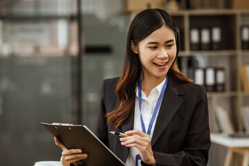 A young Asian businesswoman is seen diligently working at her desk. She's immersed in tasks ranging...