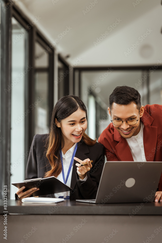 Wall mural middle-aged businessman and young asian businesswoman diligently working at desks, managing tasks as