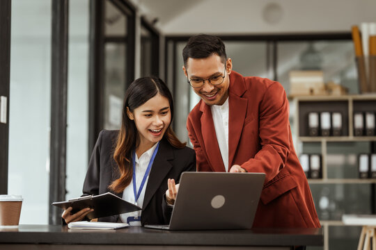 Middle-aged businessman and young Asian businesswoman diligently working at desks, managing tasks as recruitment, training, performance management, inclusive organizational culture.