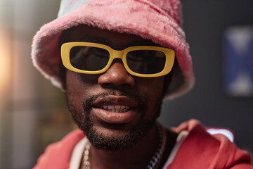 Extreme closeup portrait of Black man wearing retro sunglasses and fuzzy hat looking at camera in...