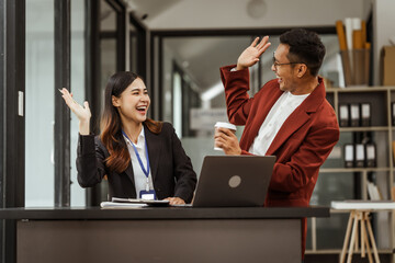 Middle-aged businessman and young Asian businesswoman diligently working at desks, managing tasks as recruitment, training, performance management, inclusive organizational culture.