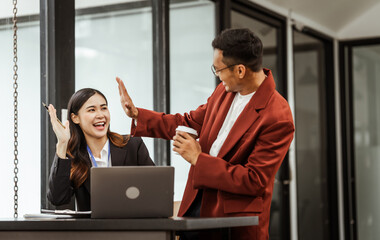 Middle-aged businessman and young Asian businesswoman diligently working at desks, managing tasks...