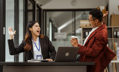 Middle-aged businessman and young Asian businesswoman diligently working at desks, managing tasks as recruitment, training, performance management, inclusive organizational culture.