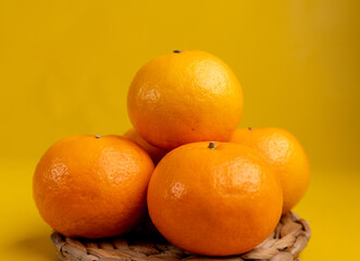 five stacked oranges on straw plate isolated yellow background