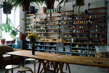 No people shot of modern pottery workshop interior with wooden furniture and ceramic products on shelves, copy space
