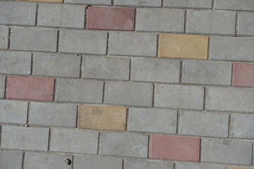 Dusty surface of gray, pink and yellow concrete pavement with stretcher bond pattern
