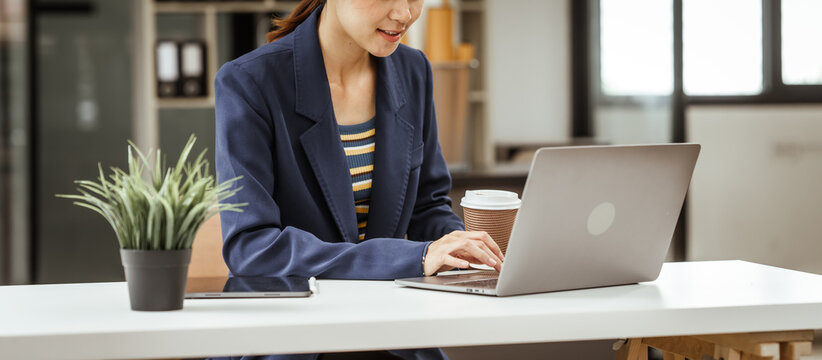 Young woman and other Asian individuals in formal suits working at desks with laptops. They engage in financial tasks including amortization, liquidity analysis, risk assessment, financial modeling.