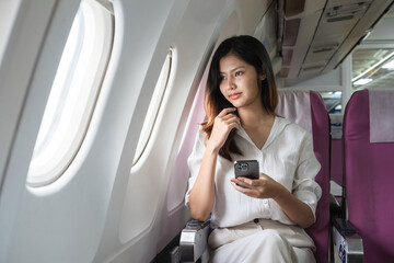 Young woman traveling on airplane and using smartphone. Concept of travel and technology
