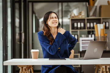 Young woman and other Asian individuals in formal suits work at desks with laptops, addressing...
