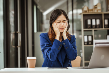 Young woman and other Asian individuals in formal suits work at desks with laptops, addressing...