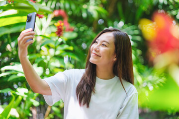 Portrait image of a young woman using mobile phone to take a selfie in the garden