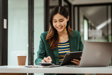 Young woman and other Asian individuals in formal suits working at desks with laptops. They engage...