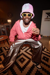 Vertical full length shot of Black young man wearing funky outfit recording dance video indoors...
