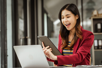 Fototapeta premium A young woman and other Asian individuals in formal suits are seen working at desks with laptops, portraying a successful and happy demeanor.