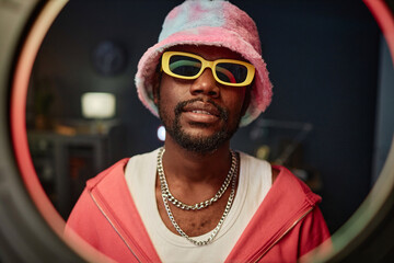 Front view portrait of trendy African American man wearing pink outfit recording videos for social...