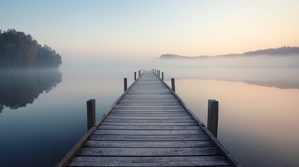 Fototapeta premium Serene wooden dock leads out over a calm lake, shrouded in soft morning mist, reflecting a peaceful and ethereal atmosphere