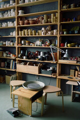 Vertical no people shot of part of pottery workshop interior with potters wheel and earthenware on shelves, copy space