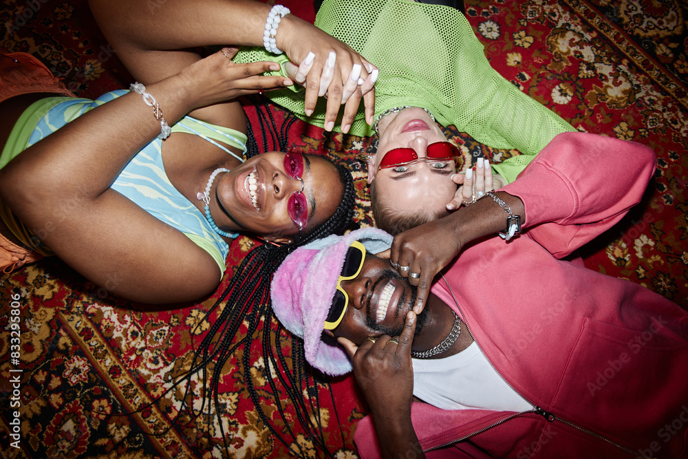 Wall mural top view of three trendy young people lying on ornate carpet in circle and looking at camera shot wi