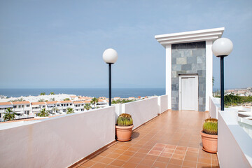 Coastal views from a high up terrace of a residential building rooftop featuring a narrow passage to an elevator shaft and two white lamps on each side in Costa Adeje, Tenerife, Canary Islands, Spain