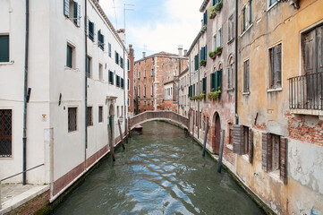 Typical scene of the unique Venetian streets and canals flanked by weathered tall buildings and connected by bridges for foot traffic, one of European most popular holiday destinations, Venice, Italy