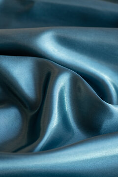 Silk fabric in a beautiful, shimmering teal-blue colour, luxurious textile with a smooth and glossy texture, highlighted by the light reflection on its surface giving it a sense of depth and elegance