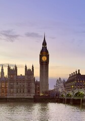 Obraz premium A view of Big Ben and the Palace of Westminster against a purple sunset sky across the River Thames at dusk in central London, England. 