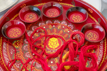 Lovely thali plate decorated with Lord Ganesha at center containing kalava strings used as protection or divine blessings and tiny bowls for the sacred ingredients part of a Hindu pre-wedding ceremony