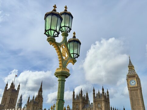 A low angle view of a vintage lamp on Westminster Bridge against a blue sky with Big Ben and the Houses of Parliament in the background, London, England. 