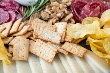 Snack platter featuring a selection of crackers, potato chips, cured salami, walnuts and thin slices of cheese part of a larger charcuterie board consumed as appetizers at parties or casual gatherings