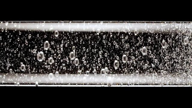 Macro shot of fine air bubbles rising in water in glass test tube on black background. Effervescent tablet aspirin. The medicine concept, health care, treatment. Slow motion. High quality FullHD 