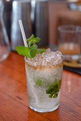 Refreshing mojito cocktail set on a bar counter ready to be served, delicious alcoholic drink prepared in a clear glass with crushed ice, fresh mint leaves and lime and garnished with a sprig of mint