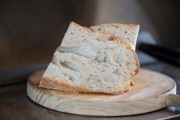 Few slices of fresh out of the oven sourdough bread set on a rustic wooden board, delicious baked loaf with a lovely texture, a golden crust and a soft and airy interior, accompaniment to many dishes