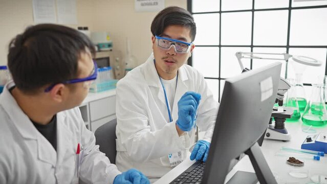 Two asian scientists discussing data on a computer in a laboratory setting.
