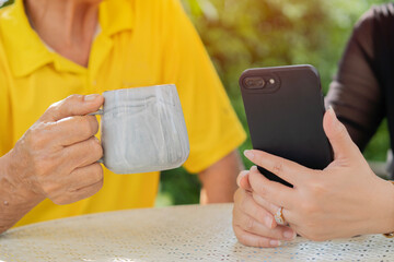 Closeup image of an Asian woman holding , using her smart phone while talking with her grandfather...