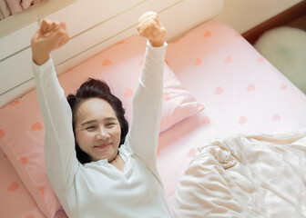 Smiling Asian lady awake after healthy sleep and laying in cozy comfortable bedroom
