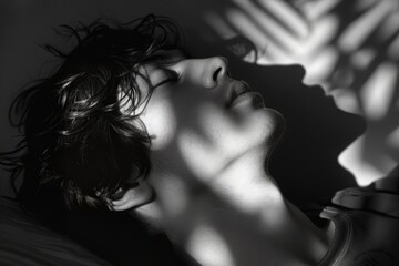 Dramatic monochrome image of a young man resting his head on a pillow, with shadows casting over his face, photo of slacker