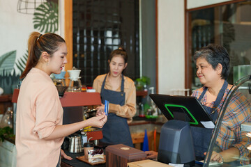 Beautiful Asian female customer holding credit card In order to pay for coffee and bakery items to An elderly single mother shop owner receives a retirement pension At the cash register counter