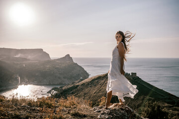 A woman in a white dress stands on a hill overlooking the ocean. The scene is serene and peaceful,...