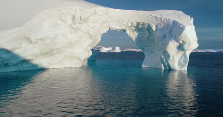 Arch in melting Arctic iceberg floating blue ocean water. Low angle drone flight in big hole white snow covered ice glacier. Ecology, conservation, melting ice, climate change, global warming concept © mozgova