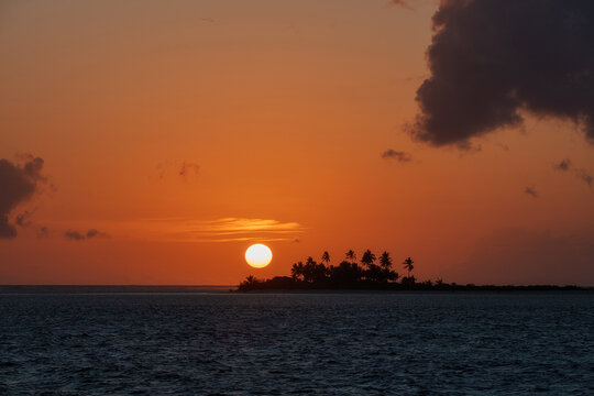 Red sunset with a silhouette of a small tropical island with palm trees in the middle of the ocean in Seychelles, Africa