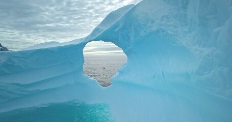 Slow motion drone fly in blue ice hole melted iceberg in Antarctica. Huge glacier drifting South pole ocean. People in boat explore Arctic winter global warming. Climate change landscape, close up