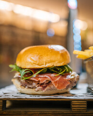 Gourmet Burger with Prosciutto and Fresh Greens on a Wooden Plate