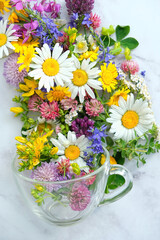 colorful flowers and herbs in glass cup on table close up. floral tea, organic healthy beverage. Flavor useful herbal tea from natural wild plants. alternative medicine concept. top view