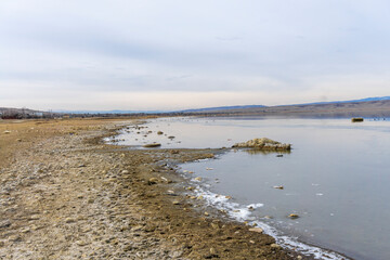 Dirty lake shore, dead fish on the ice. Disturbed ecology. Mountains in the background