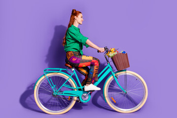 Full size photo of good mood woman dressed green shirt vintage pants riding bike in empty space isolated on purple color background