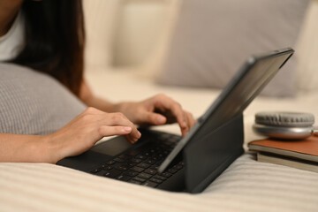 Fototapeta premium Cropped shot relaxed young woman lying on bed at home, using digital tablet