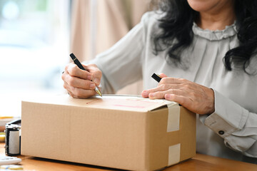 Close up senior female entrepreneur writing address on cardboard for delivery to customers