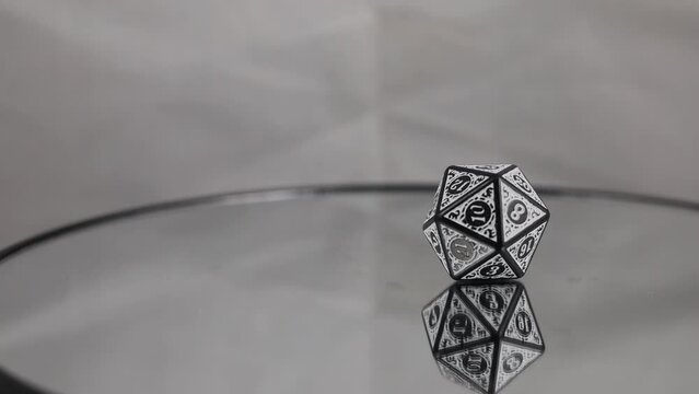 A D20 or 20-sided white die with black prints spinning on a mirrored turntable