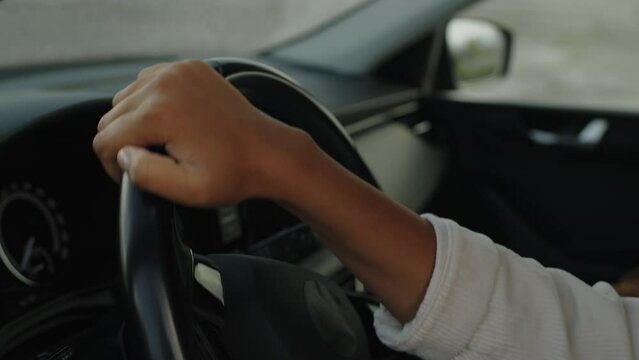 Close-up of anonymous young female learner driver practising in turning steering wheel and alternating hands, while taking lesson with professional instructor