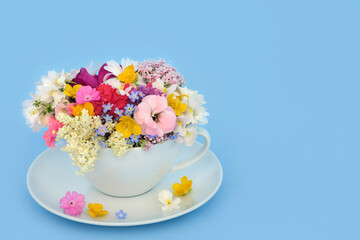 Surreal summer flowers and wildflowers teacup decoration on blue background. Floral fun abstract food medicinal nature surrealism design.